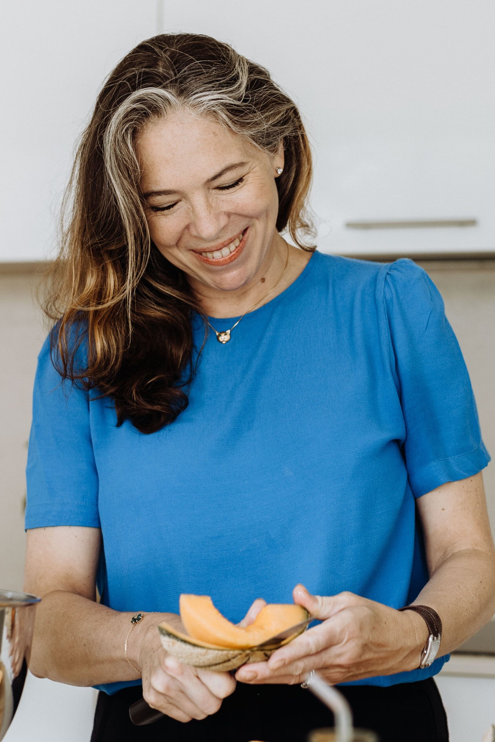 Jessica Fonteneau, Registered Nutritional Therapist and eczema specialist - white woman with long, mid-brown hair, smiling, wearing a blue top and peeling melon.